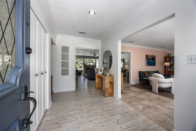 foyer entrance with visible vents, light wood-style flooring, ornamental molding, a textured ceiling, and a fireplace