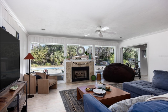 living area featuring a fireplace, a ceiling fan, crown molding, and wood finished floors