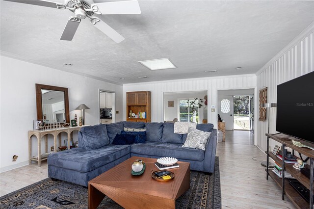 living area with ornamental molding, light wood-type flooring, a textured ceiling, and a skylight