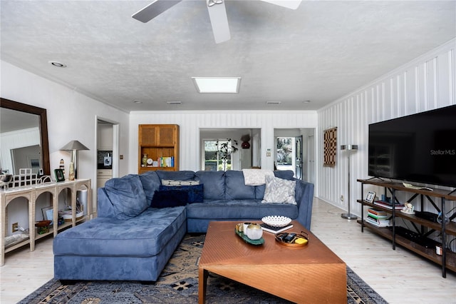 living area with light wood-type flooring, ceiling fan, ornamental molding, and a textured ceiling