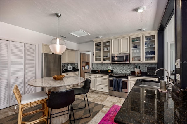 kitchen featuring stainless steel appliances, a sink, backsplash, and cream cabinets