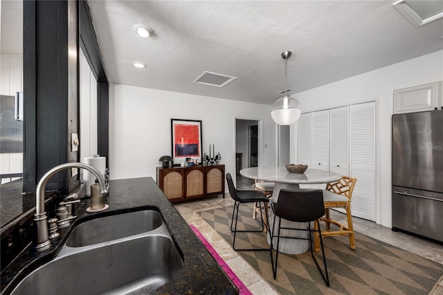 kitchen with light tile patterned flooring, a sink, freestanding refrigerator, dark stone countertops, and pendant lighting