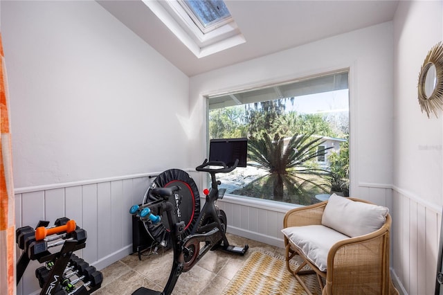 workout area with a wainscoted wall and vaulted ceiling with skylight