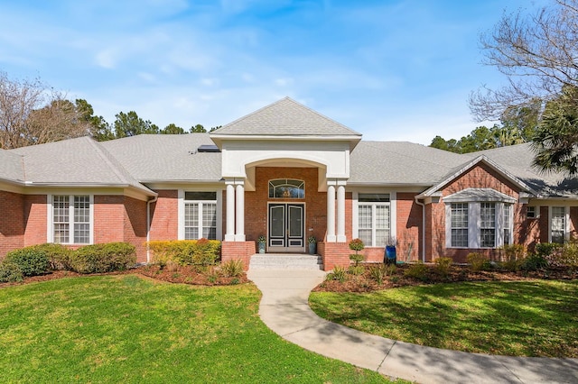 view of front of property featuring a front yard, brick siding, and roof with shingles