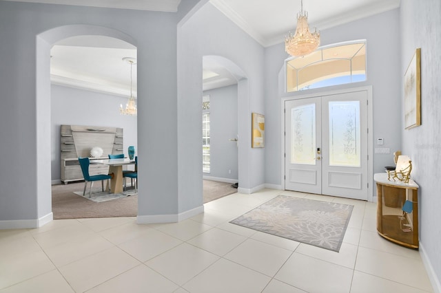 entrance foyer featuring baseboards, a chandelier, arched walkways, and crown molding