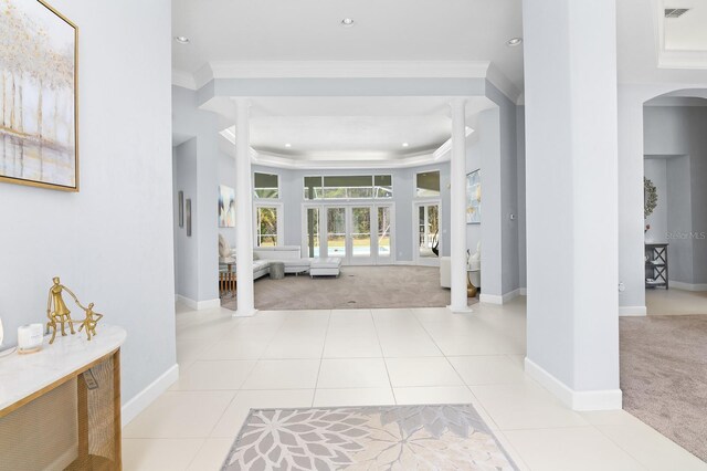 carpeted foyer entrance featuring a tray ceiling, ornamental molding, tile patterned floors, and ornate columns