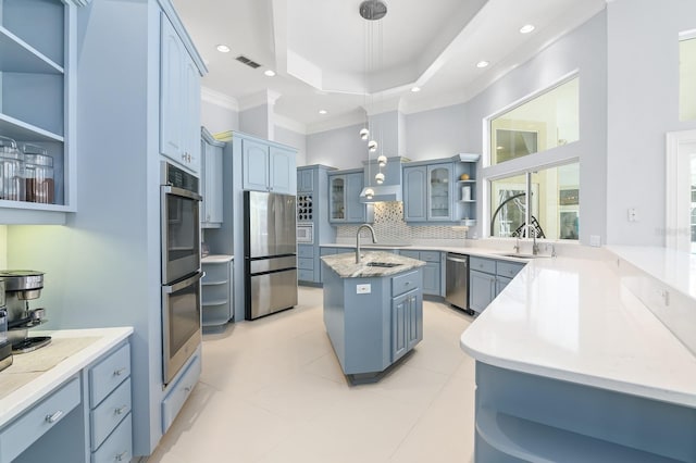 kitchen with open shelves, a raised ceiling, decorative backsplash, appliances with stainless steel finishes, and a kitchen island with sink