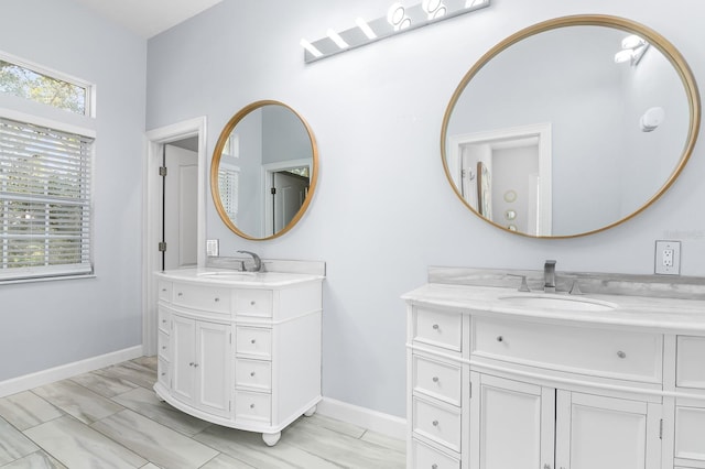 full bath featuring baseboards, two vanities, and a sink