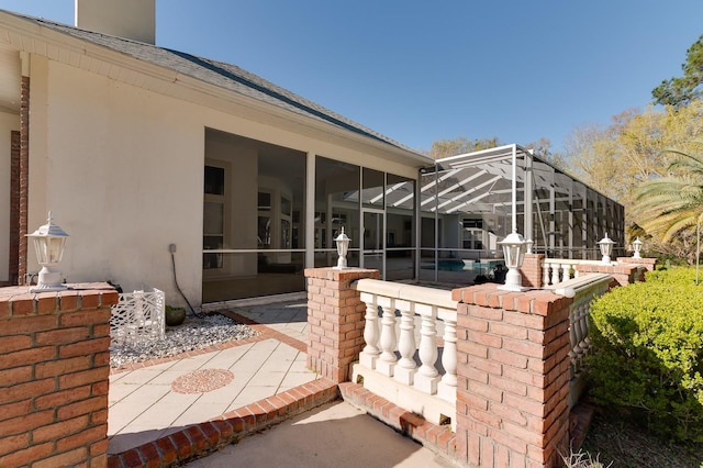 rear view of property featuring glass enclosure, a shingled roof, a patio, and stucco siding