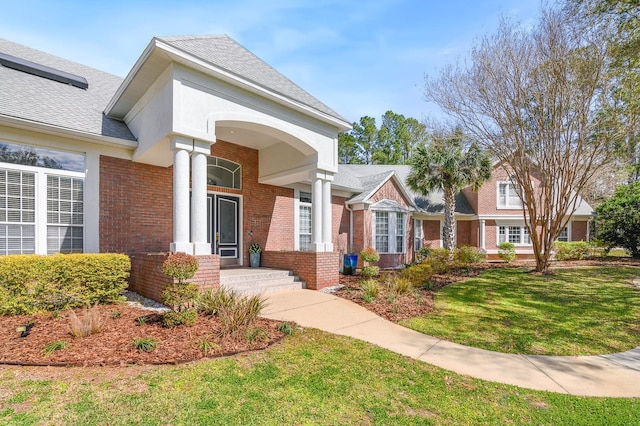 view of front of house featuring a shingled roof, brick siding, and a front lawn