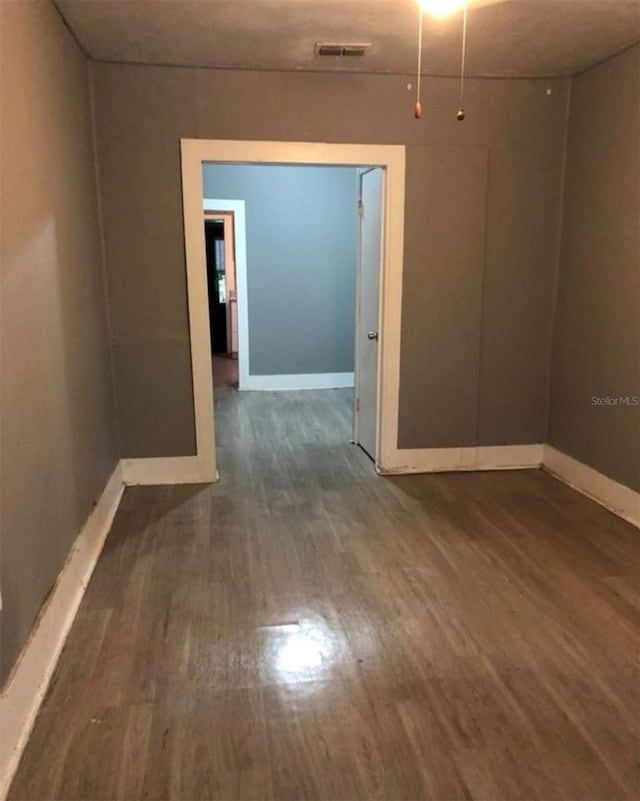 empty room featuring wood finished floors, visible vents, and baseboards