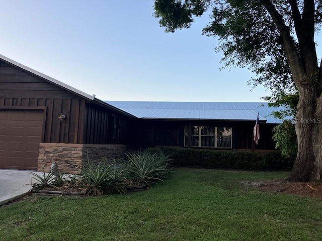 view of front of home with board and batten siding, a front yard, stone siding, and an attached garage