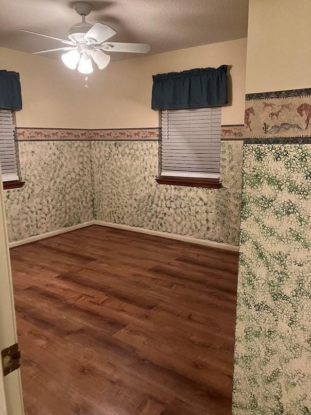 spare room with ceiling fan, a textured ceiling, wood finished floors, wainscoting, and wallpapered walls