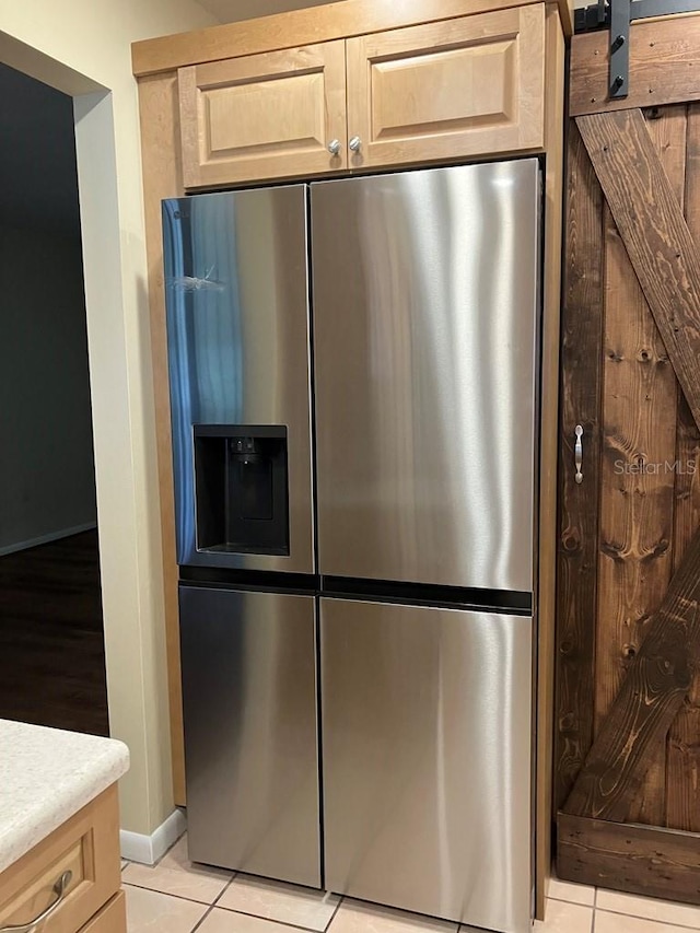 kitchen with light tile patterned floors, stainless steel fridge, a barn door, light countertops, and light brown cabinetry