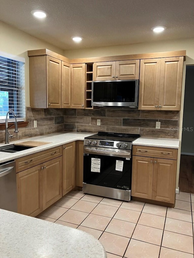 kitchen featuring stainless steel appliances, light countertops, backsplash, light tile patterned flooring, and a sink