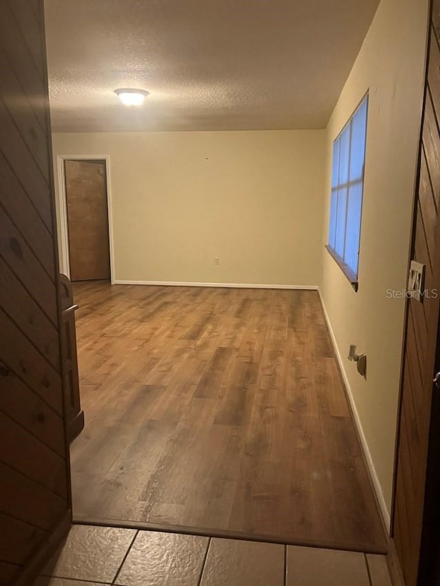 empty room featuring a textured ceiling, wood finished floors, and baseboards