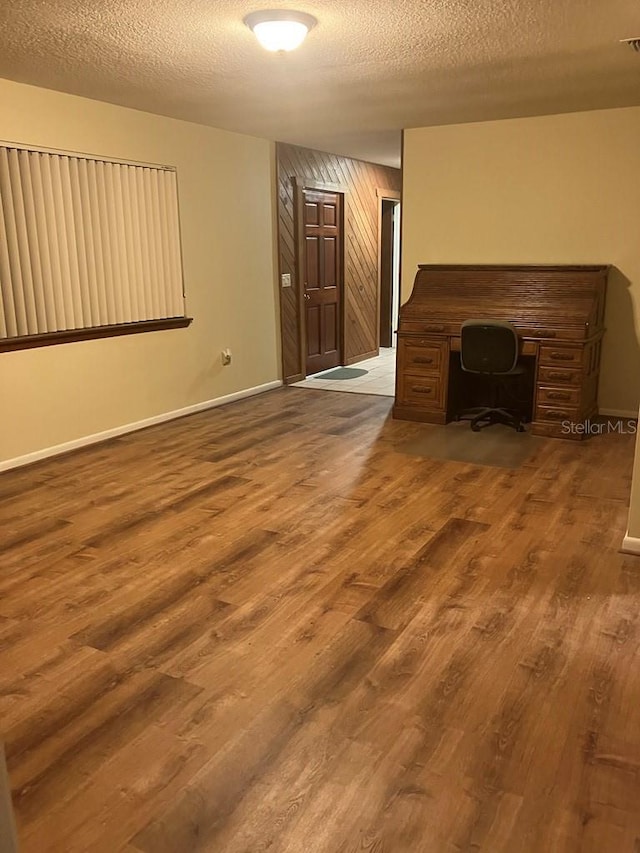 unfurnished living room with a textured ceiling, wood walls, wood finished floors, and baseboards