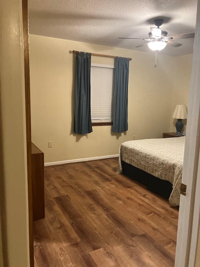 bedroom with a textured ceiling, wood finished floors, and baseboards