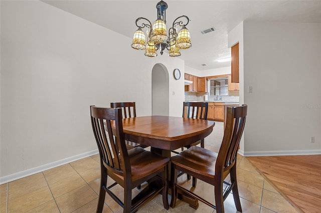 dining area featuring baseboards, visible vents, arched walkways, a chandelier, and light tile patterned flooring