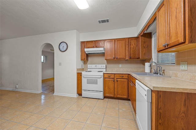 kitchen with white appliances, brown cabinets, a sink, and under cabinet range hood