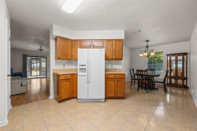 kitchen featuring white fridge with ice dispenser, brown cabinetry, visible vents, and light tile patterned floors