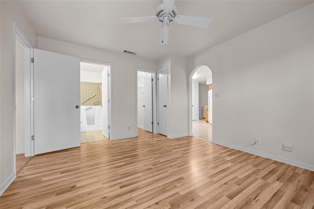 unfurnished bedroom featuring arched walkways, connected bathroom, visible vents, and light wood-style floors