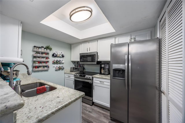 kitchen with light stone counters, appliances with stainless steel finishes, dark wood-type flooring, white cabinetry, and a sink