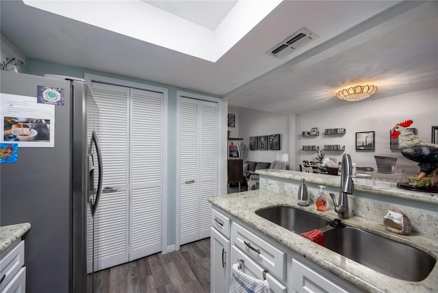 kitchen with dark wood-style flooring, stainless steel refrigerator with ice dispenser, visible vents, white cabinetry, and a sink