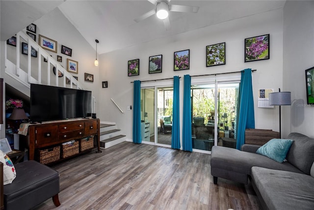 living area with high vaulted ceiling, wood finished floors, a ceiling fan, baseboards, and stairway