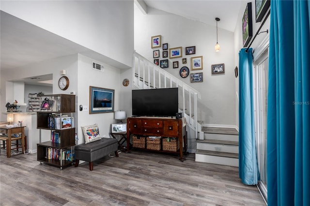 living area featuring high vaulted ceiling, visible vents, stairway, and wood finished floors