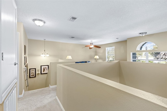 corridor featuring a textured ceiling, light colored carpet, visible vents, baseboards, and an upstairs landing