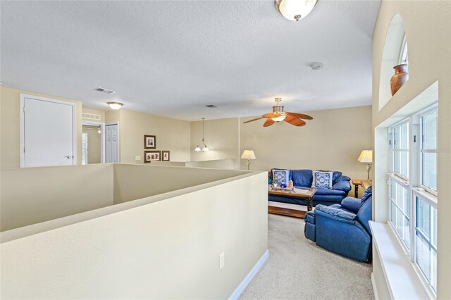 hall featuring carpet floors, visible vents, a textured ceiling, and an upstairs landing