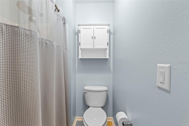 full bath featuring toilet, a shower with curtain, and a textured wall