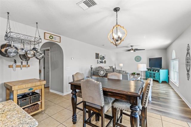 dining space with arched walkways, light tile patterned floors, visible vents, baseboards, and a ceiling fan