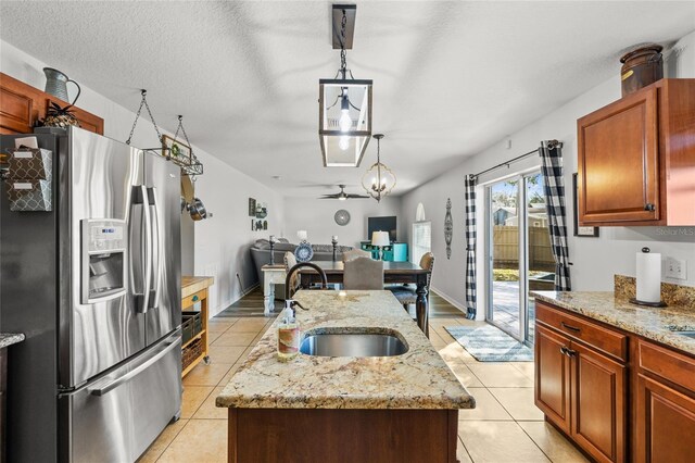 kitchen with light tile patterned flooring, a sink, hanging light fixtures, stainless steel fridge with ice dispenser, and a center island with sink