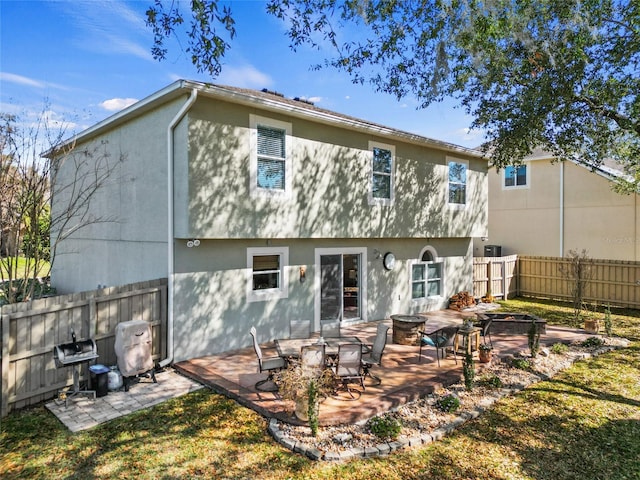 rear view of house with an outdoor fire pit, a patio area, fence, and stucco siding