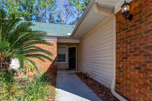 property entrance with roof with shingles and brick siding