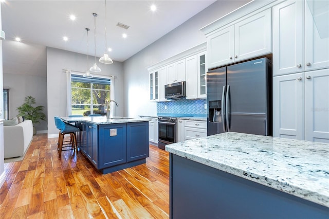kitchen featuring light stone counters, stainless steel appliances, a sink, visible vents, and tasteful backsplash