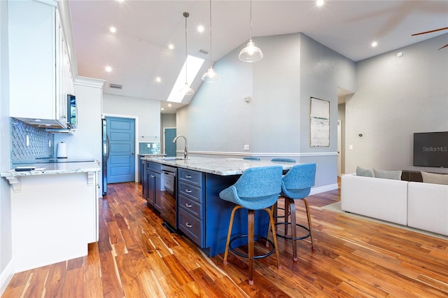 kitchen featuring high vaulted ceiling, blue cabinets, wood finished floors, white cabinetry, and a kitchen bar