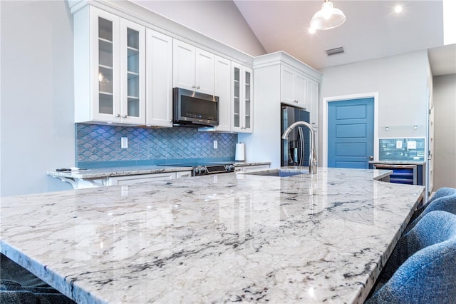 kitchen featuring light stone counters, a breakfast bar, white cabinetry, appliances with stainless steel finishes, and backsplash