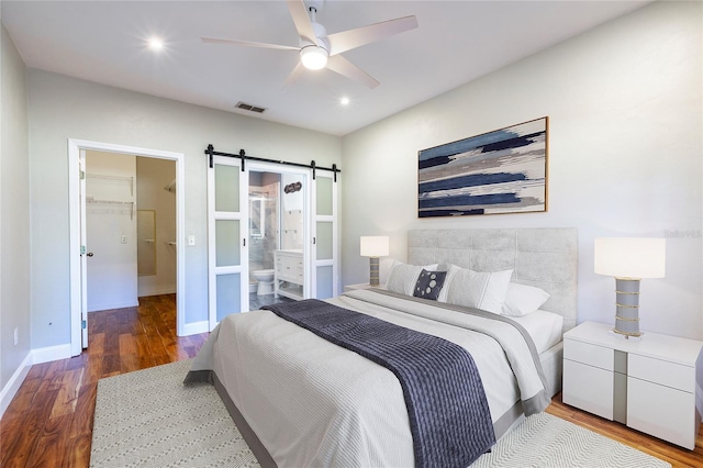 bedroom with a walk in closet, visible vents, a barn door, connected bathroom, and wood finished floors