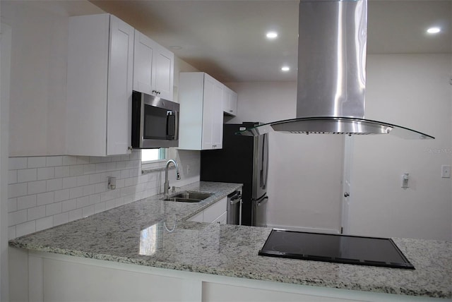 kitchen featuring stainless steel microwave, light stone countertops, cooktop, island exhaust hood, and a sink