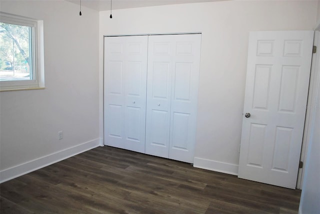 unfurnished bedroom with a closet, baseboards, and dark wood-style flooring