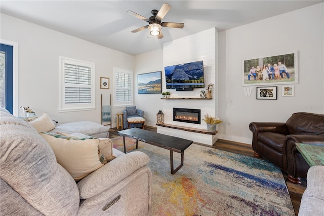 living room featuring a ceiling fan, baseboards, wood finished floors, and a glass covered fireplace