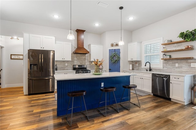 kitchen with a center island, stainless steel appliances, light countertops, wall chimney range hood, and a sink