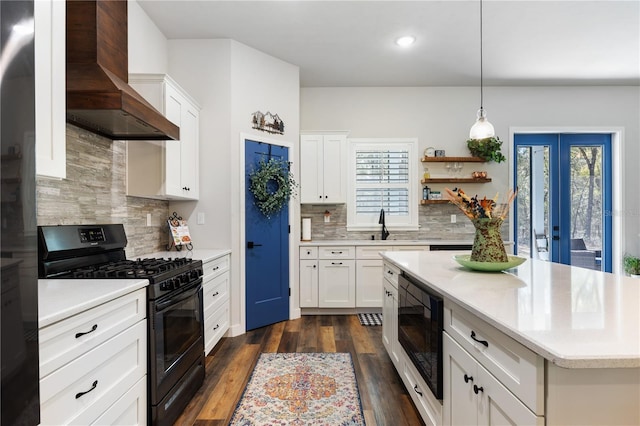 kitchen with wall chimney exhaust hood, dark wood-style flooring, light countertops, black appliances, and a wealth of natural light