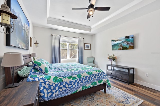 bedroom featuring a ceiling fan, baseboards, a raised ceiling, and wood finished floors