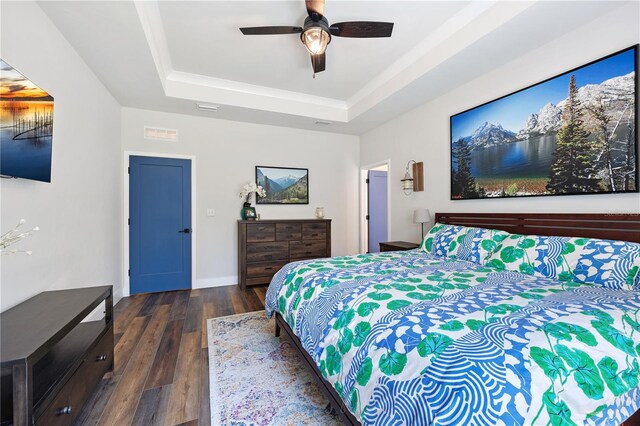 bedroom with a tray ceiling, dark wood finished floors, visible vents, a ceiling fan, and baseboards