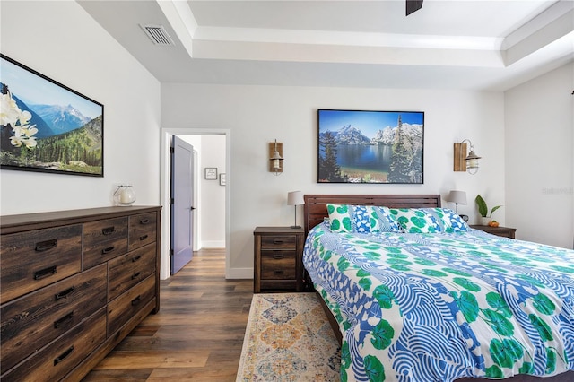 bedroom with dark wood-style floors, a raised ceiling, visible vents, and baseboards