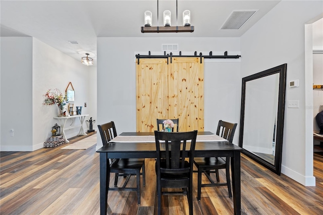 dining space featuring baseboards, a barn door, visible vents, and wood finished floors